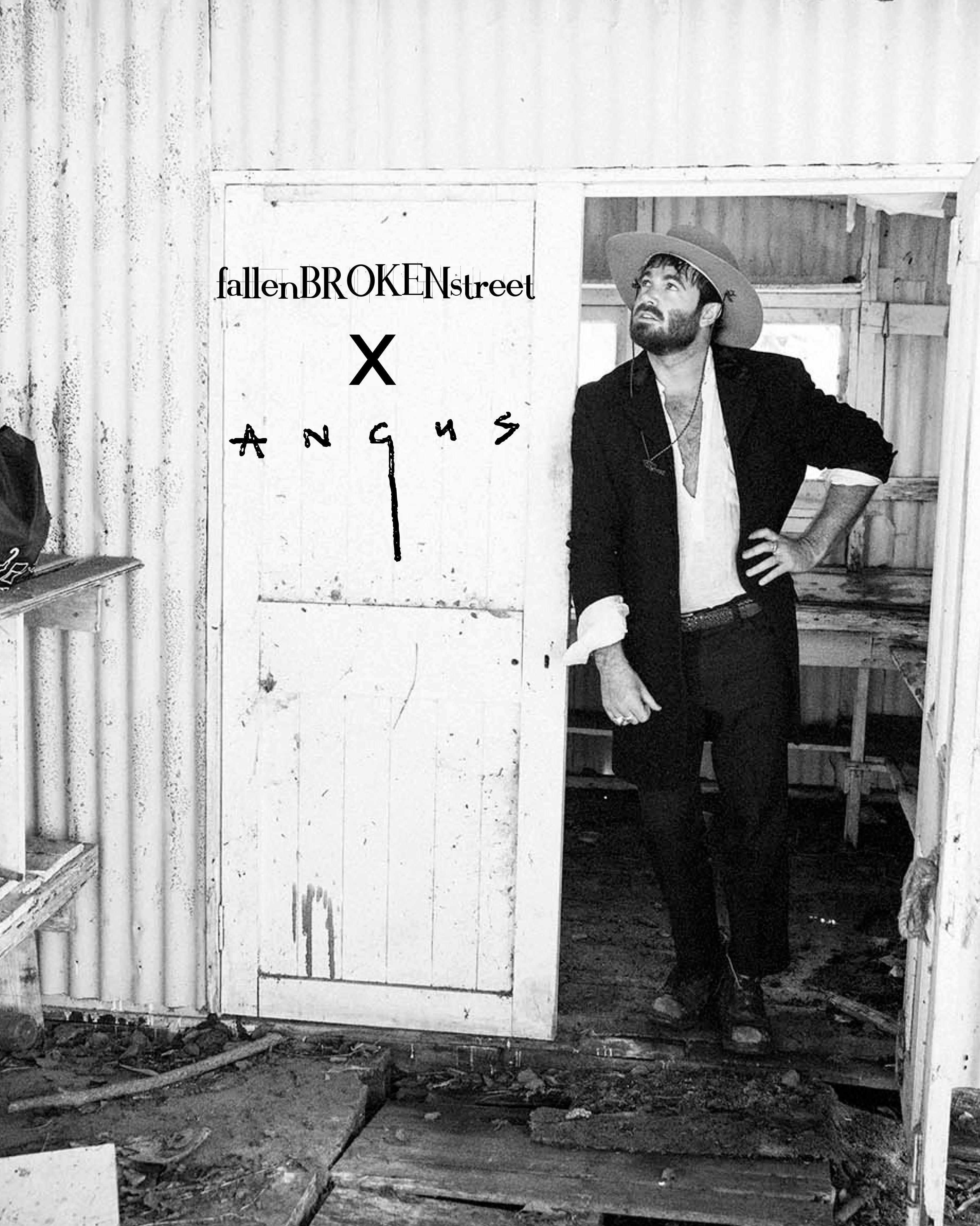 Musician Angus Stone stands in the doorway of a weathered shed wearing a felt hat from the FBS x Angus collaboration. Black and white campaign image featuring the Fallenbrokenstreet x Angus Stone logo on the door, evoking rustic, poetic energy.