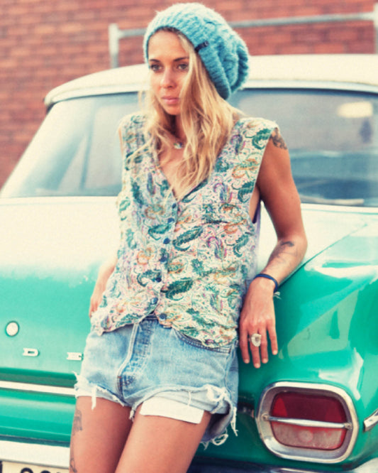 Model wears The Consciousness Beanie – Blue with a vintage outfit, standing in front of a mint green car. Casual and cozy vibe, highlighting the hat’s everyday style.