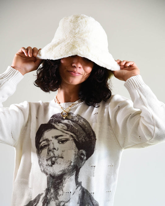 Model adjusting the brim of the white faux fur Cosmic Girl Bucket Hat. Styled with a graphic sweatshirt for a playful and nostalgic look, the soft bucket hat offers a cozy touch and fashion-forward silhouette.