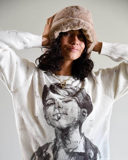 Model wears The Cosmic Girl Bucket Hat in Tan Faux Fur with a relaxed pose, hands behind head. Styled with a graphic long-sleeve top, this image showcases the hat’s ultra-soft faux fur texture and everyday wearability. The neutral tan color complements winter layers and adds a nostalgic, cosmic feel to any outfit.