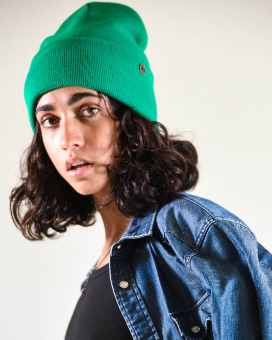 Model wearing The Lucks Beanie in green, styled with a denim jacket. FallenBROKENstreet wool blend beanie with ribbed knit pattern and folded cuff. Signature logo badge detail adds subtle branding. Designed for warmth, comfort, and unisex styling, this beanie offers a versatile fit for both city streets and festival nights.