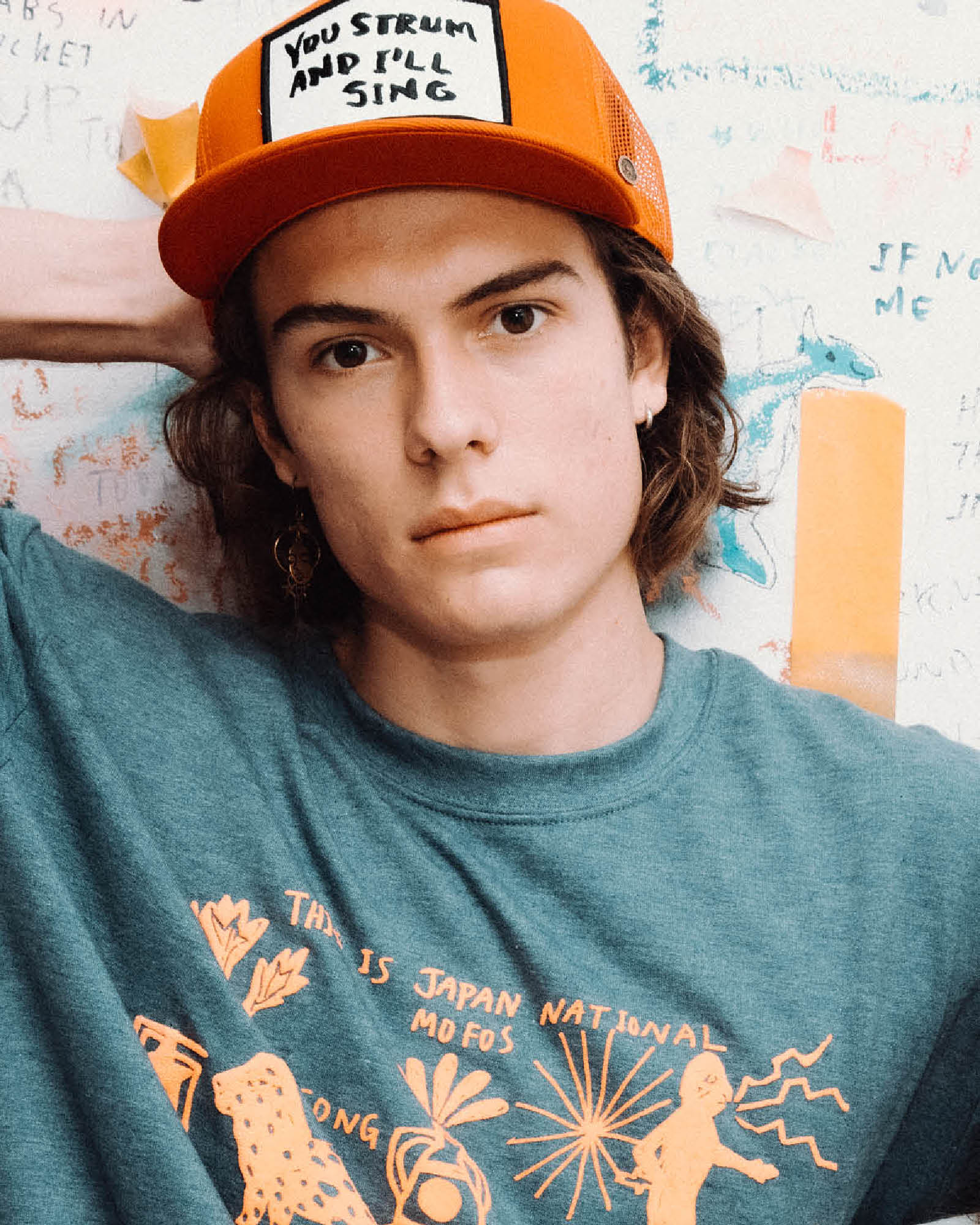 Model wearing red Marty Baptist x FallenBROKENstreet trucker cap with graphic t-shirt – lifestyle image