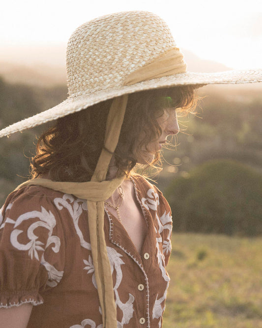 Young girl wears The Lover Straw Hat in natural straw, shown from the side against a warm afternoon light. Ideal for nature play, picnics, and long beach days.