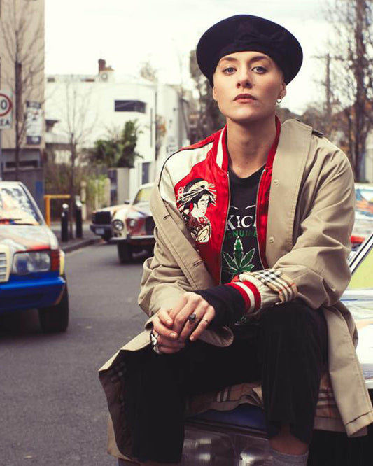Model wearing The Minnie Beret by FallenBROKENstreet in city street scene. Black wool beret with red pom-pom, signature button, and relaxed modern fit.