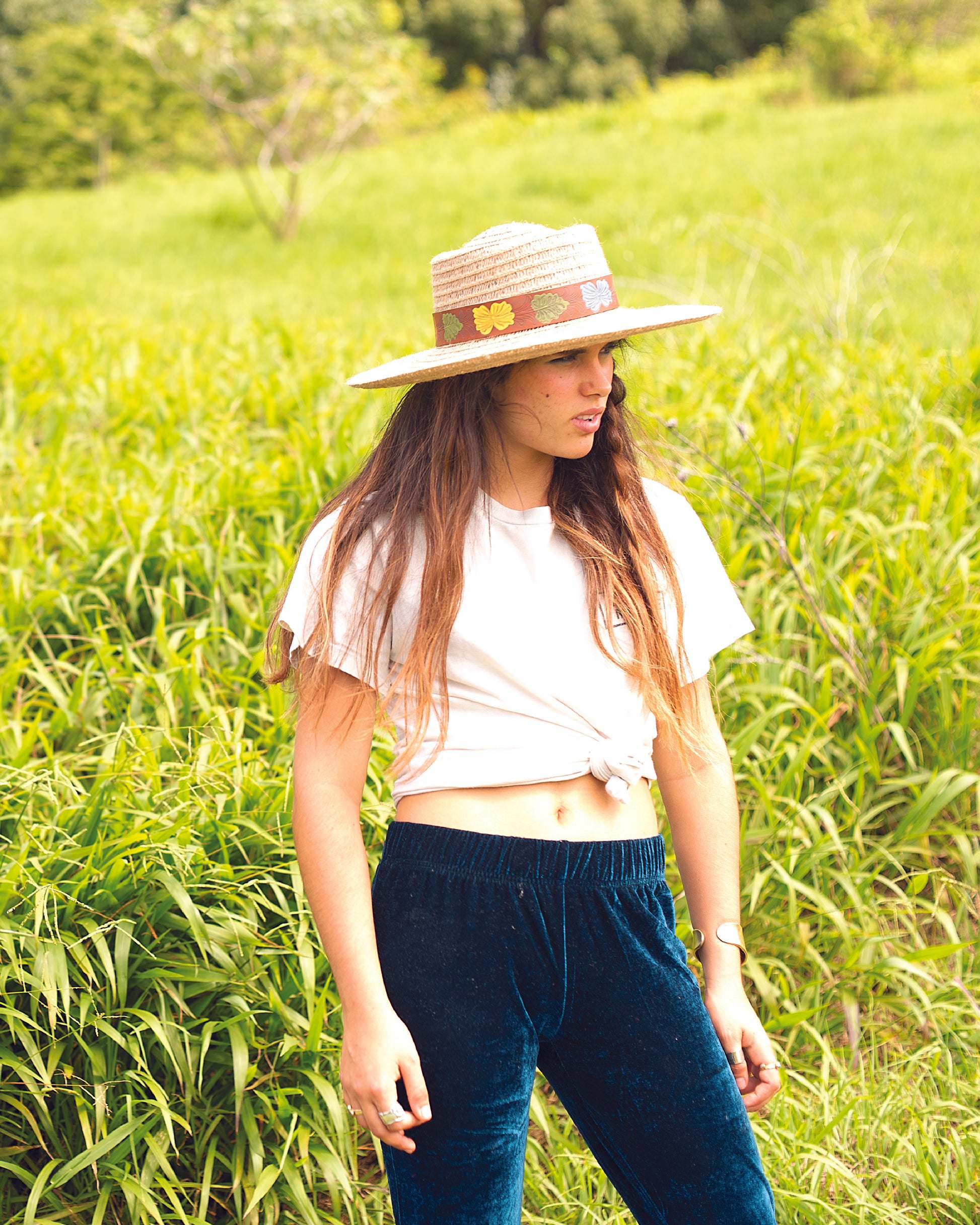 Woman wearing The Wanderer straw hat in a grassy field, styled with a white tee and navy pants – Fallenbrokenstreet.
