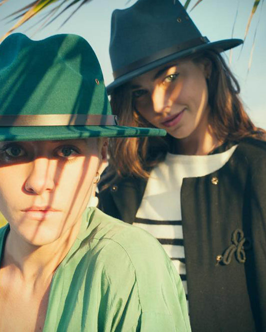 Two models wearing the FallenBROKENstreet Ratatat Felt Fedora – Real, photographed at The David Bromley Estate. Handcrafted from 100% Australian wool felt with a leather band and metal button detail. Unisex design styled with green outerwear in natural light.