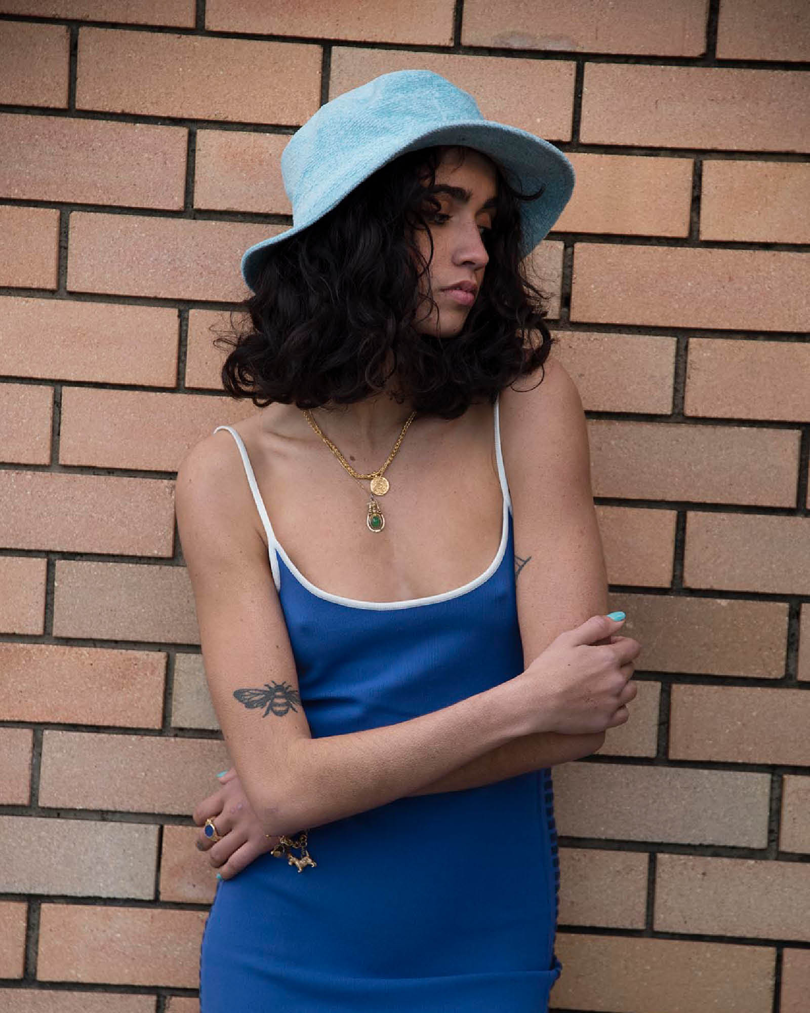 Portrait shot of model wearing the Saturday Bucket Hat – Blue. Lightweight cotton chenille with wide brim, breathable cotton inner band, and UPF 50+ rating. A bright unisex summer essential for festivals, beach days, and streetwear styling.