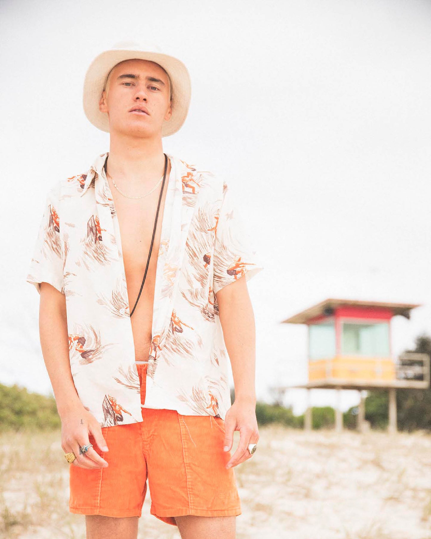 Full-body portrait of model wearing Saturday Bucket Hat – White by FallenBROKENstreet. Lightweight cotton chenille hat with wide brim and UPF 50+ protection. Styled casually with floral shirt and shorts, photographed by the coast, emphasising its travel and summer-ready versatility.