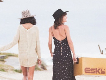 Two women walk up the beach wearing fallen broken street womens felt hats