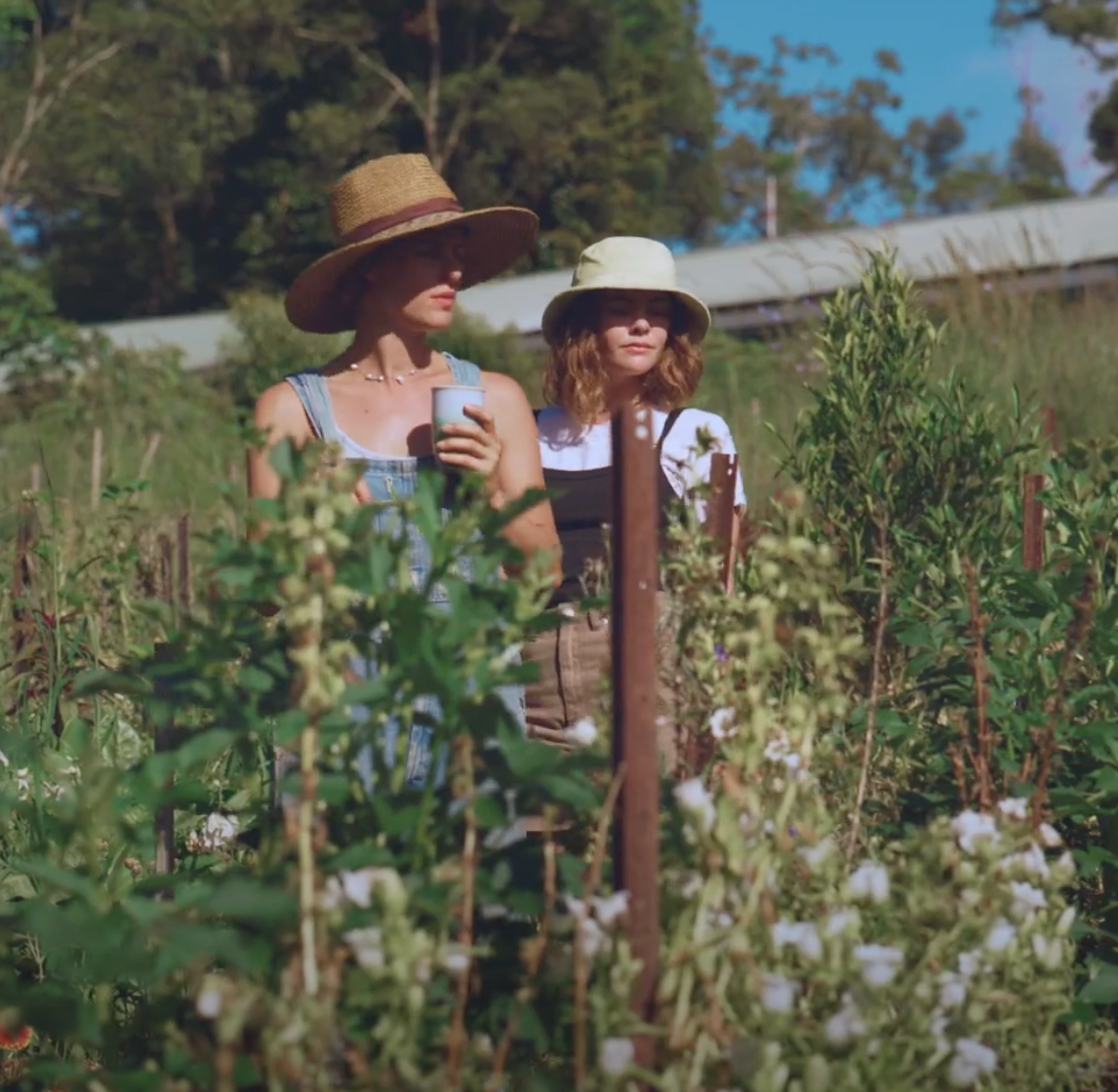Two women wearing fallen broken street women straw hats walk through a garden near Byron Bay nsw. One women wears a Brown  womens Straw hat and the other wears a lime bucket hat