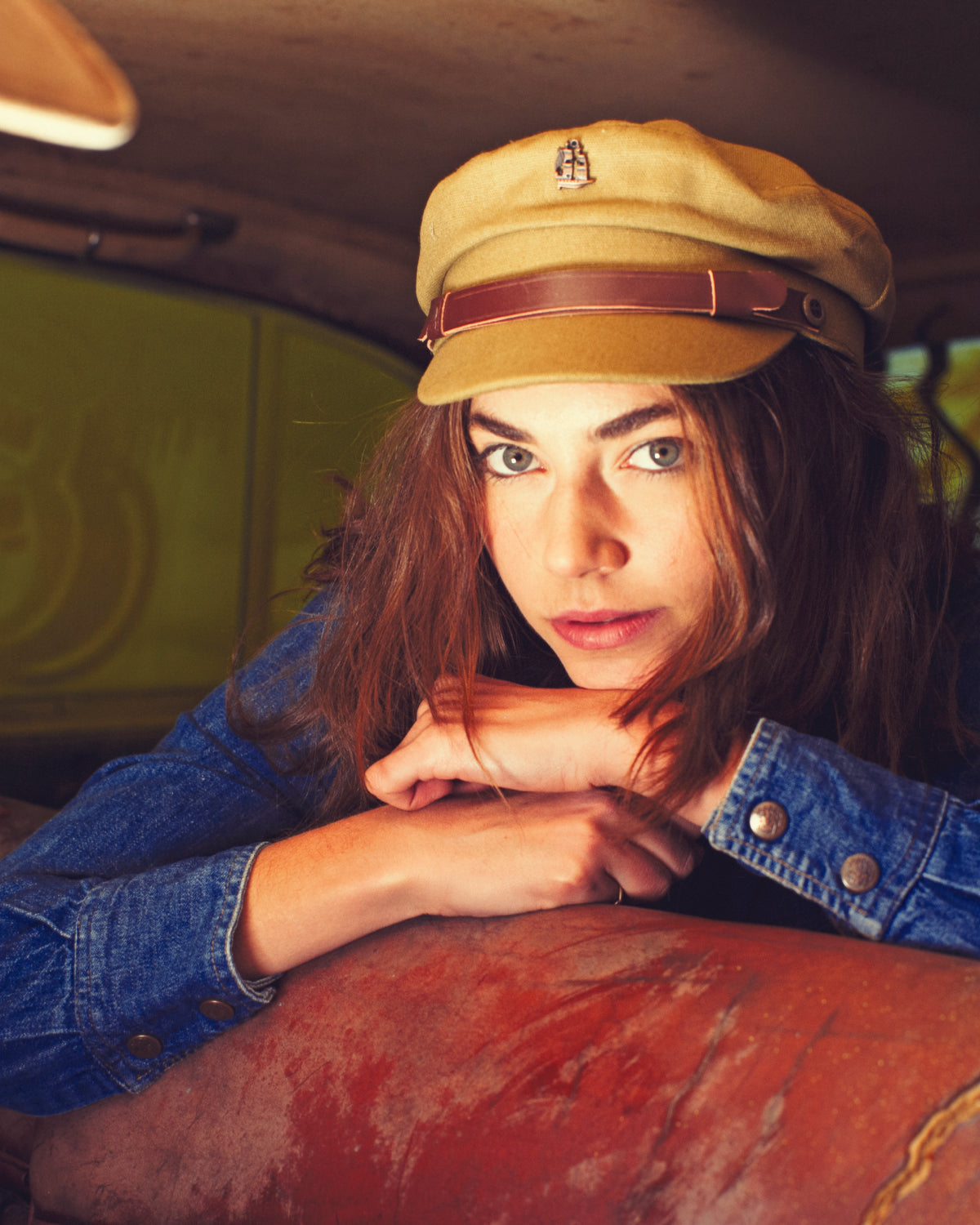 A women wears a fallen broken street fisherman cap while sitting in the back seat of a vintage car.