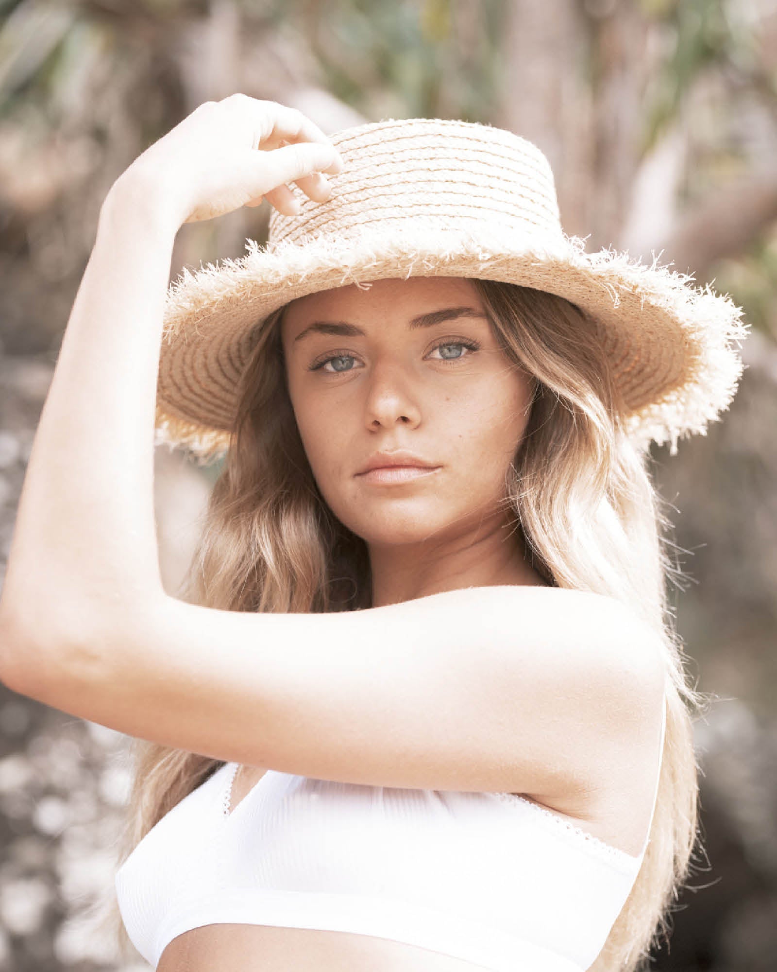 A closer shot of the model adjusting The Seeker Straw Hat, focusing on the frayed edge and the raw organic texture of the raffia straw.