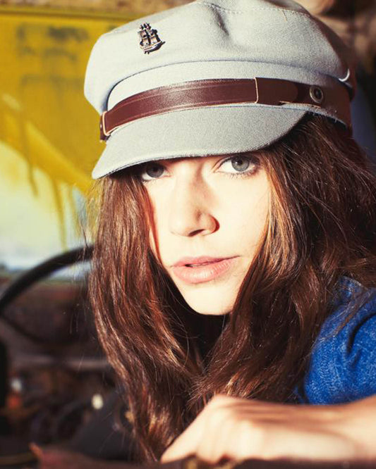 Model wearing The Sea Cap – Steel by FallenBROKENstreet, styled with deep blue sweater in vintage car interior. Canvas sailor cap with leather band and ocean-inspired detailing.