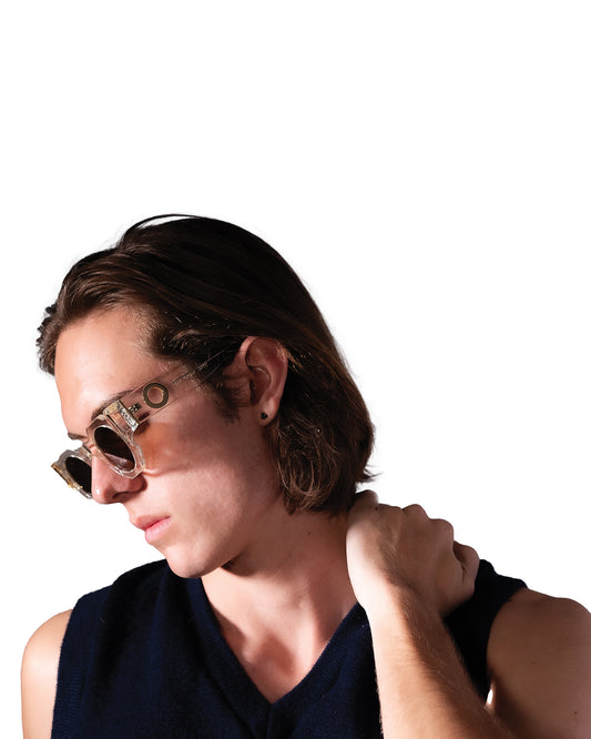 Model with tousled hair wears Fallenbrokenstreet's The Cosmos sunglasses in Skywalker/Black. Featuring black lenses and translucent acetate frames with subtle gold detail, this image highlights both elegance and edge. A strong lifestyle image to communicate mood and fit.