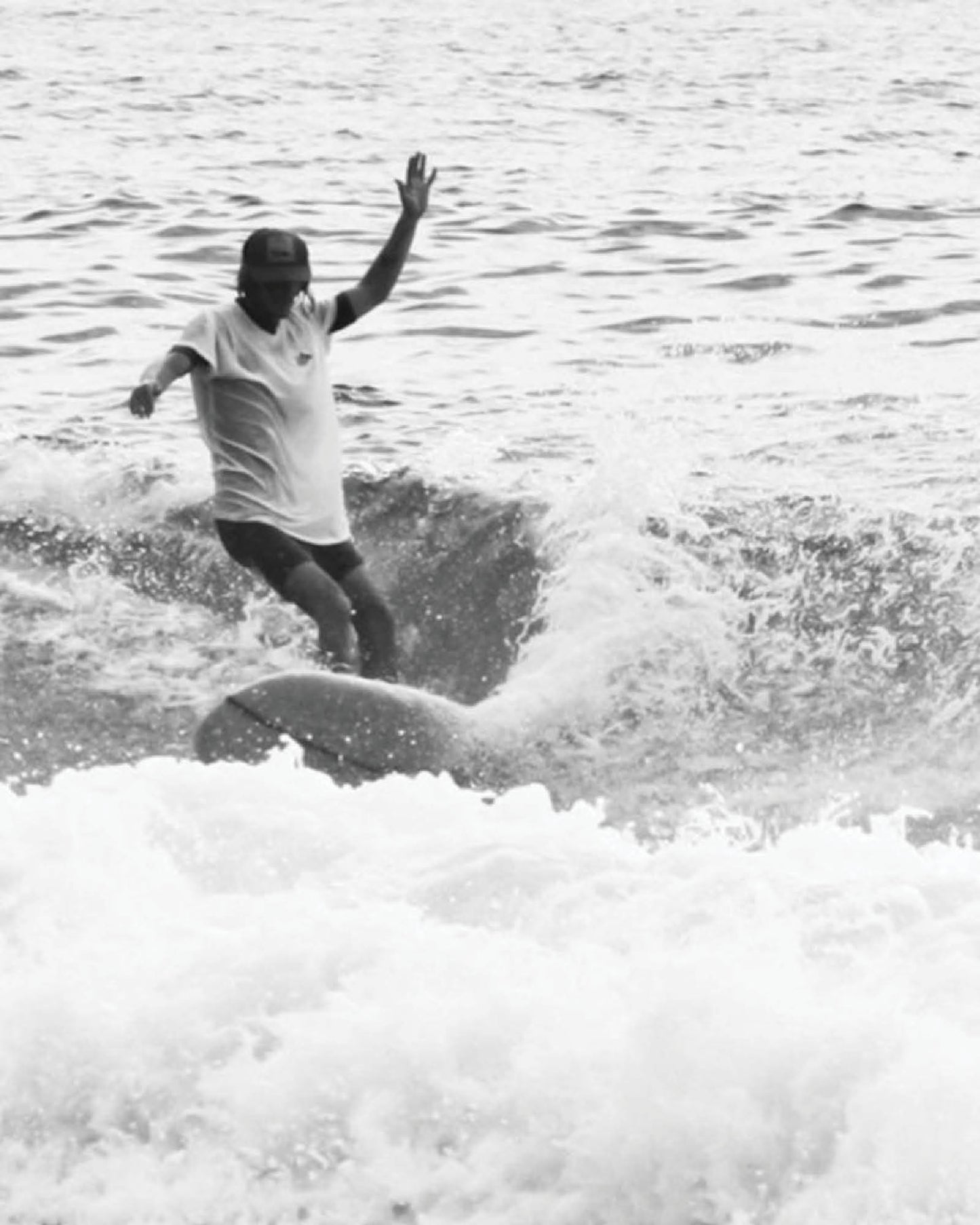 A surfer rides a wave in Byron Bay wearing the Surf Stash Cap by FallenBROKENstreet. Captured in black and white, the image reflects coastal lifestyle and freedom, with the hidden stash pocket design perfect for travel and festivals. The Surf Stash Cap – Red combines surf culture with timeless streetwear style for beach days and beyond.