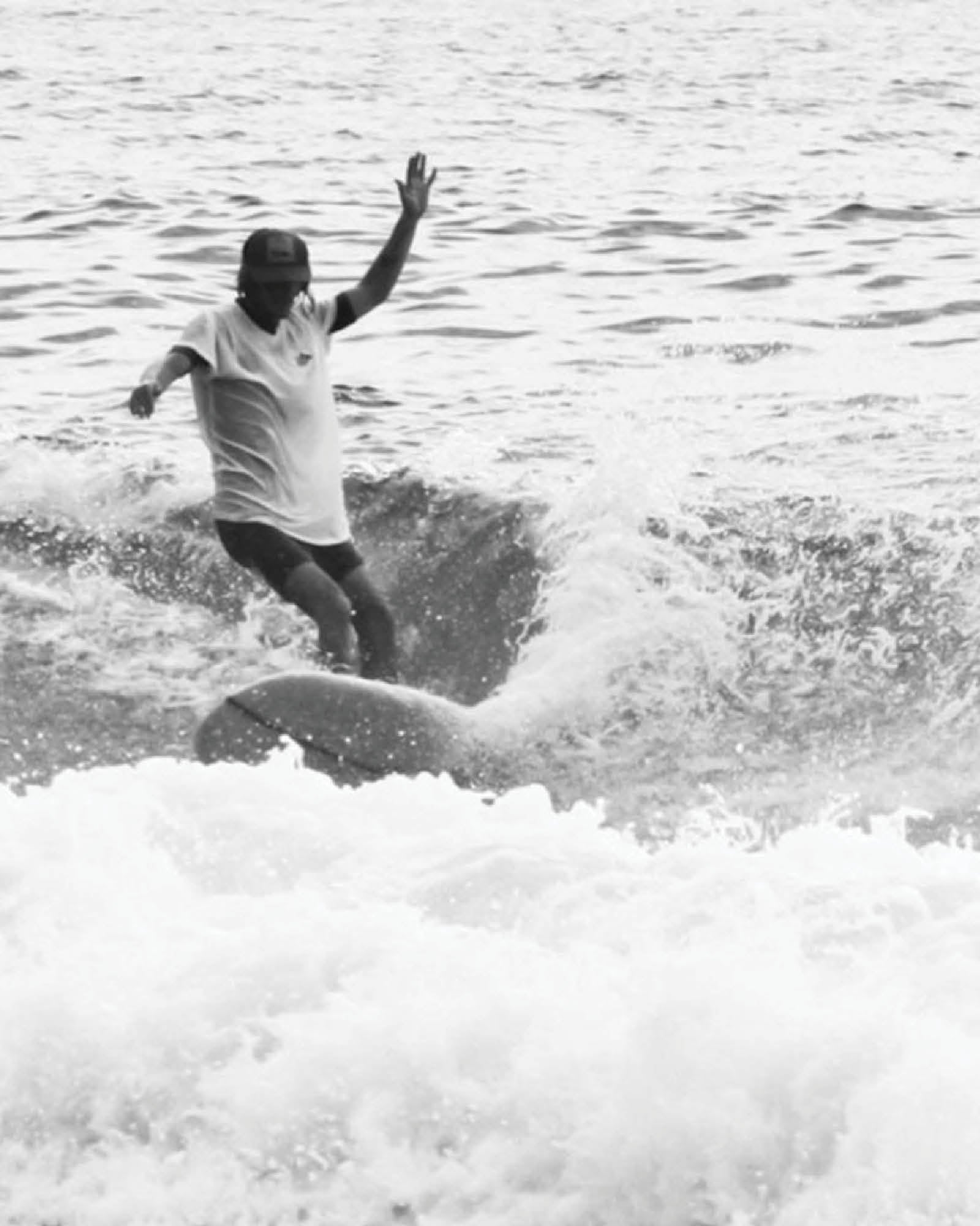 A surfer rides a wave in Byron Bay wearing the Surf Stash Cap by FallenBROKENstreet. Captured in black and white, the image reflects coastal lifestyle and freedom, with the hidden stash pocket design perfect for travel and festivals. The Surf Stash Cap – Red combines surf culture with timeless streetwear style for beach days and beyond.