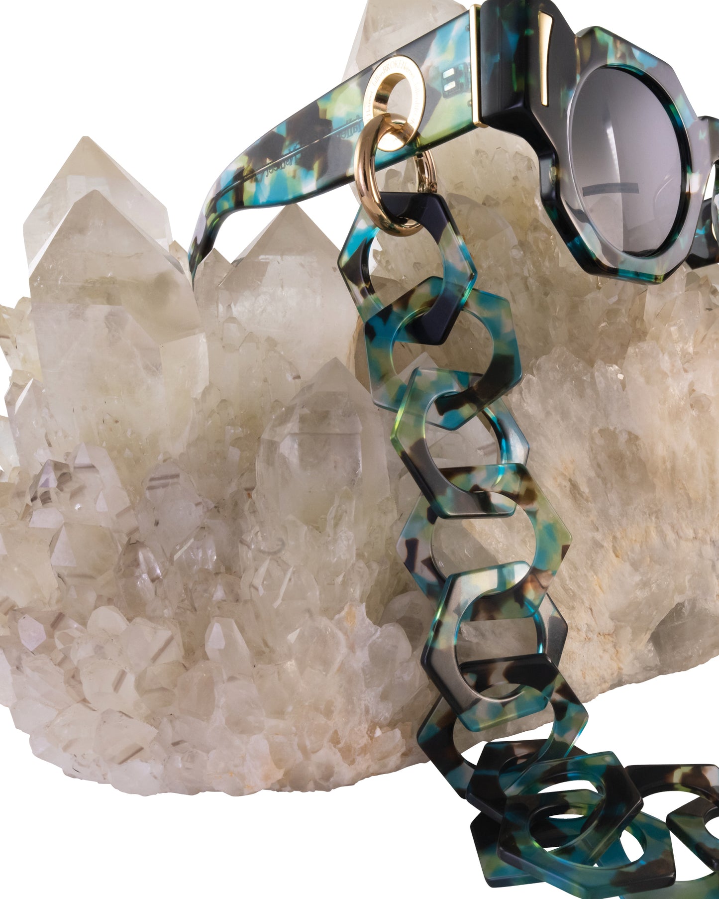 Lifestyle product photo of THE COSMOS – Galaxy/Black sunglasses displayed on a natural quartz crystal cluster. Highlights the cosmic theme and artistic presentation.