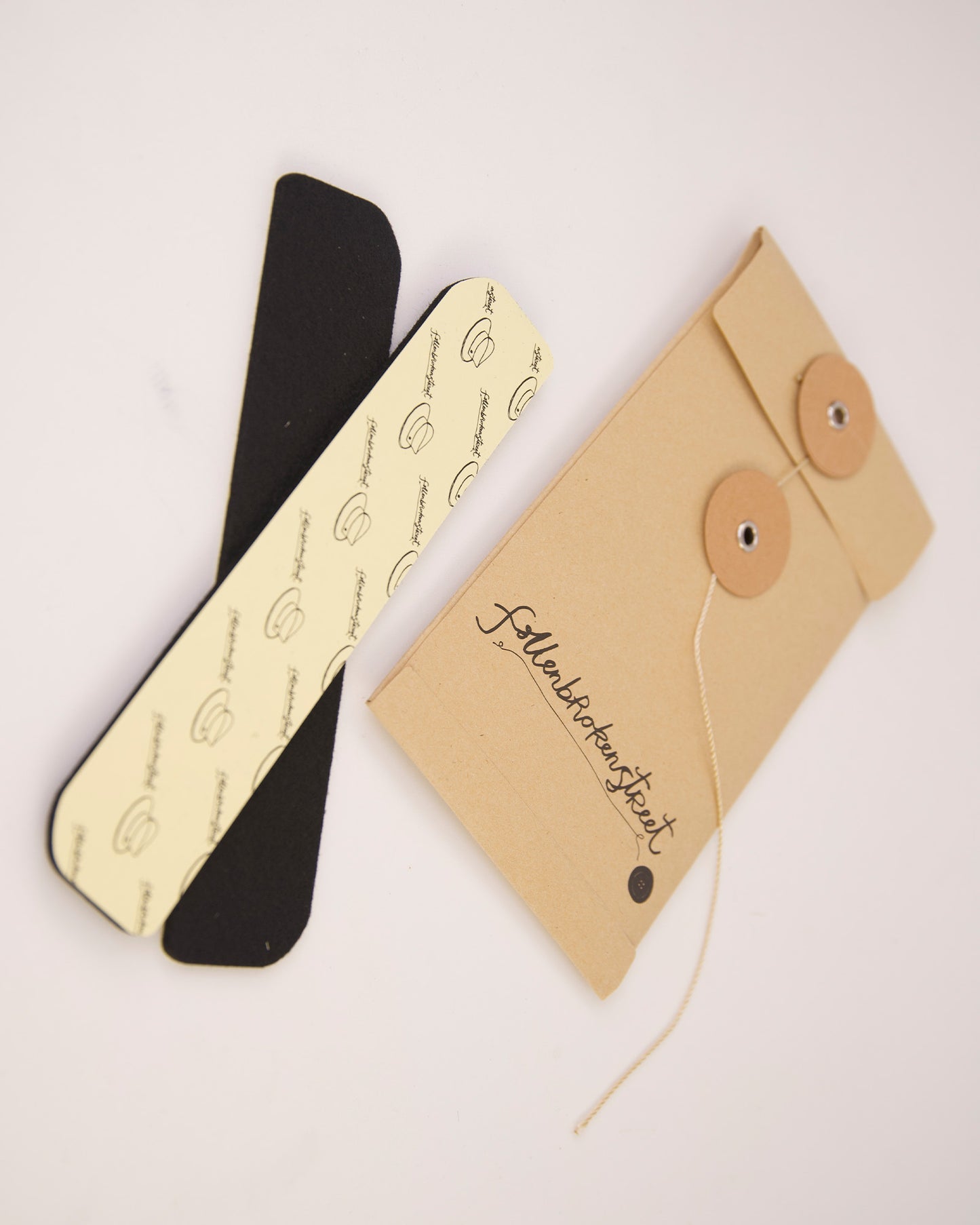 Flat-lay image showing both adhesive hat filler strips next to branded packaging. Designed by Fallenbrokenstreet, these felt strips help reduce hat size subtly and effectively. Stick them under the sweatband for a custom snug fit, especially useful for in-between sizes or styling preferences. The neutral colours match any interior and stay hidden when worn. A clean, aesthetic product presentation suitable for online shopping galleries and detailed product pages.