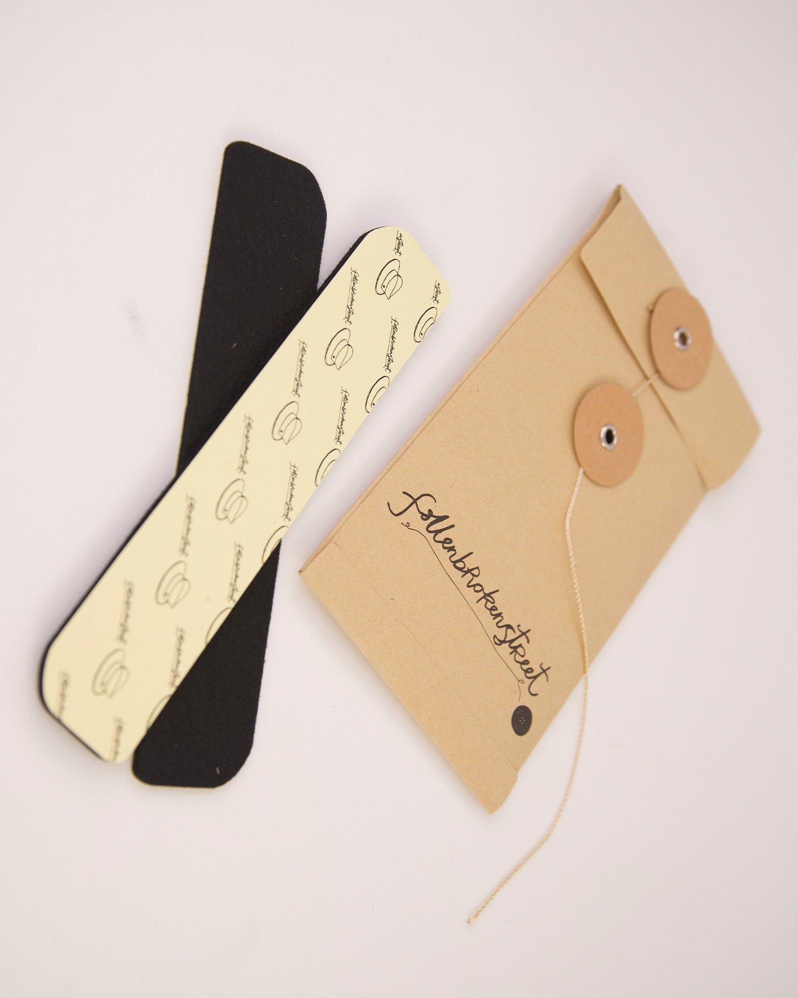 Flat-lay image showing both adhesive hat filler strips next to branded packaging. Designed by Fallenbrokenstreet, these felt strips help reduce hat size subtly and effectively. Stick them under the sweatband for a custom snug fit, especially useful for in-between sizes or styling preferences. The neutral colours match any interior and stay hidden when worn. A clean, aesthetic product presentation suitable for online shopping galleries and detailed product pages.
