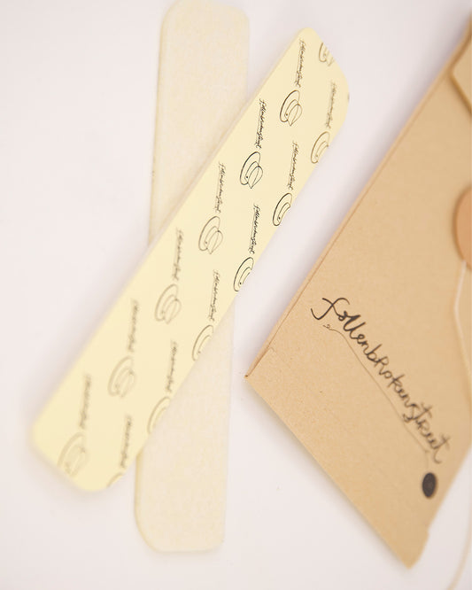 Flat-lay showing two natural felt hat filler strips with branded Fallenbrokenstreet kraft paper tag. Each strip measures 16cm and includes strong adhesive backing for easy placement under the hat lining. A simple and effective solution for hat wearers needing size adjustment or better grip. Presented with clean aesthetic for online store visuals.