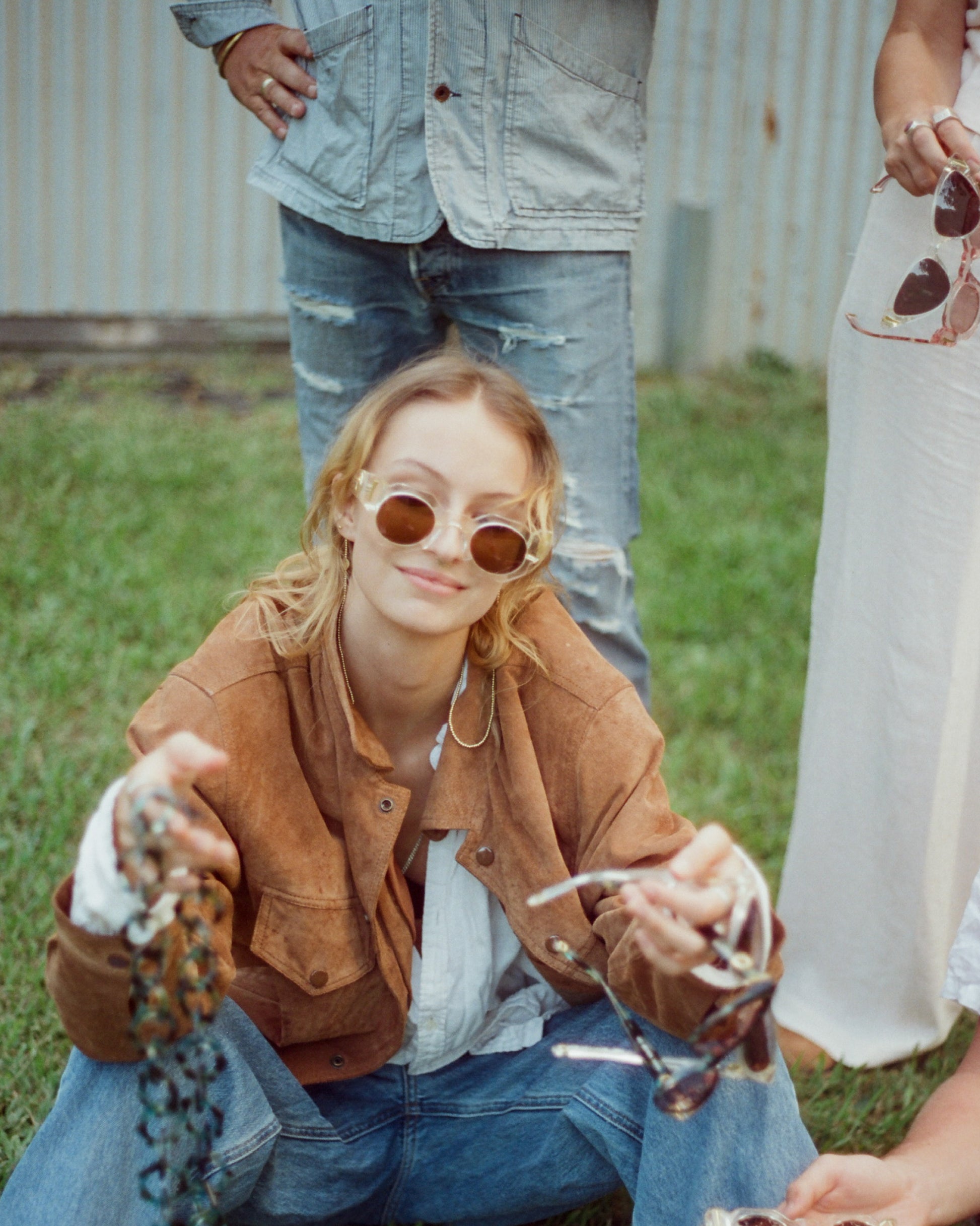 On-ground seated image of model in Skywalker/Amber sunglasses. Smiling with friends, capturing carefree vibe and laid-back attitude. Highlights real-life styling and comfort fit of the shades.
