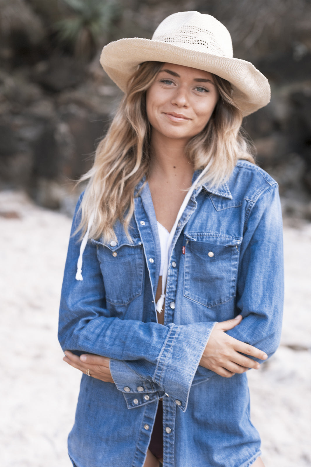 Outdoor lifestyle shot featuring a model in double denim wearing The Lover Straw Hat in Natural. Captures a carefree bohemian mood, with soft light filtering through trees, evoking freedom, sun-drenched days, and Australian summer spirit.