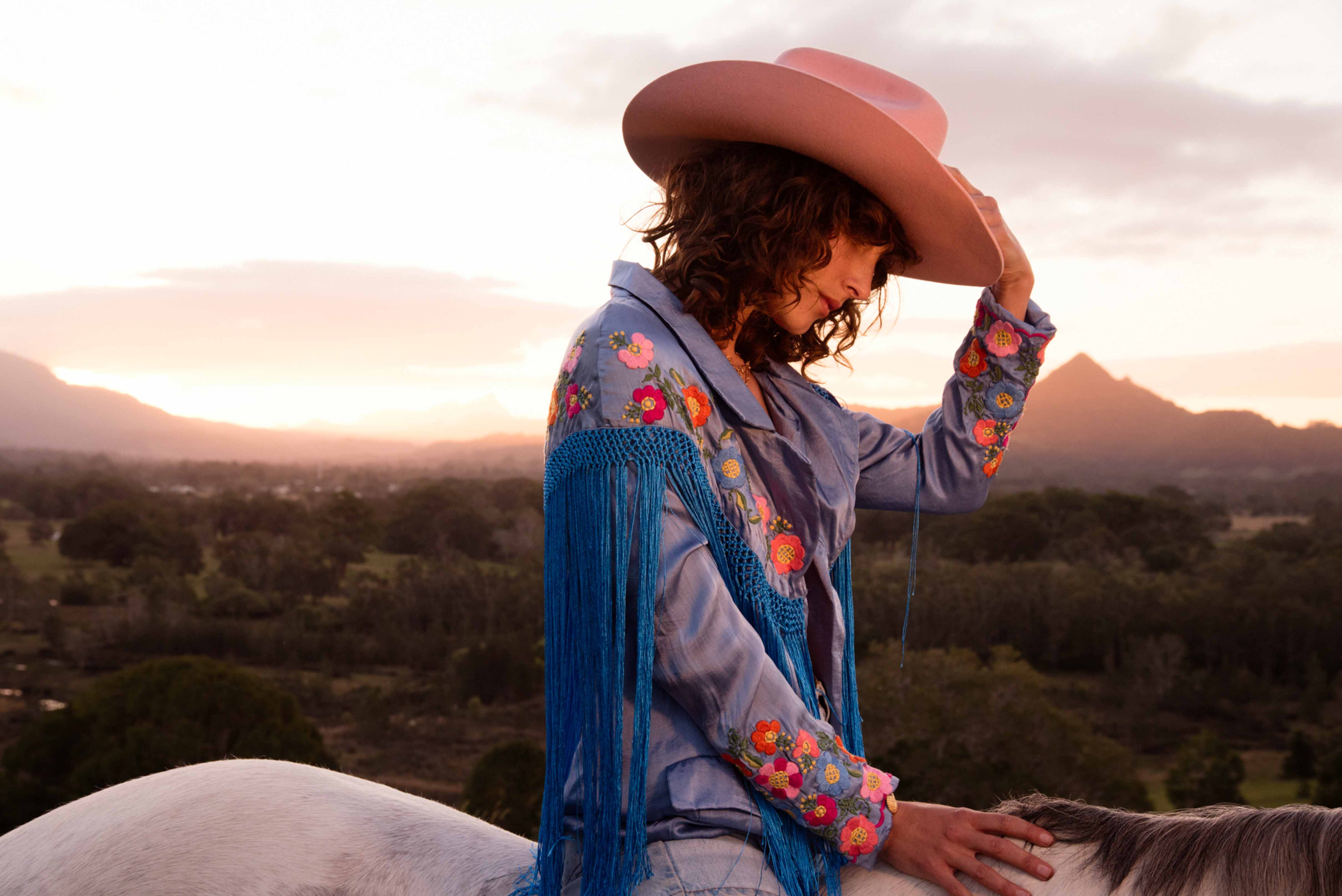 Model in blush pink Fallenbrokenstreet cowboy hat, wide brim wool felt, riding at golden hour with mountain view, modern cowboy style.