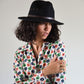 Woman wearing a black hat and a colorful floral shirt against a plain background