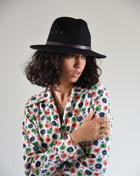 Woman wearing a black hat and a colorful floral shirt against a plain background