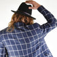 Person wearing a blue checkered jacket and black fedora, facing away from the camera.