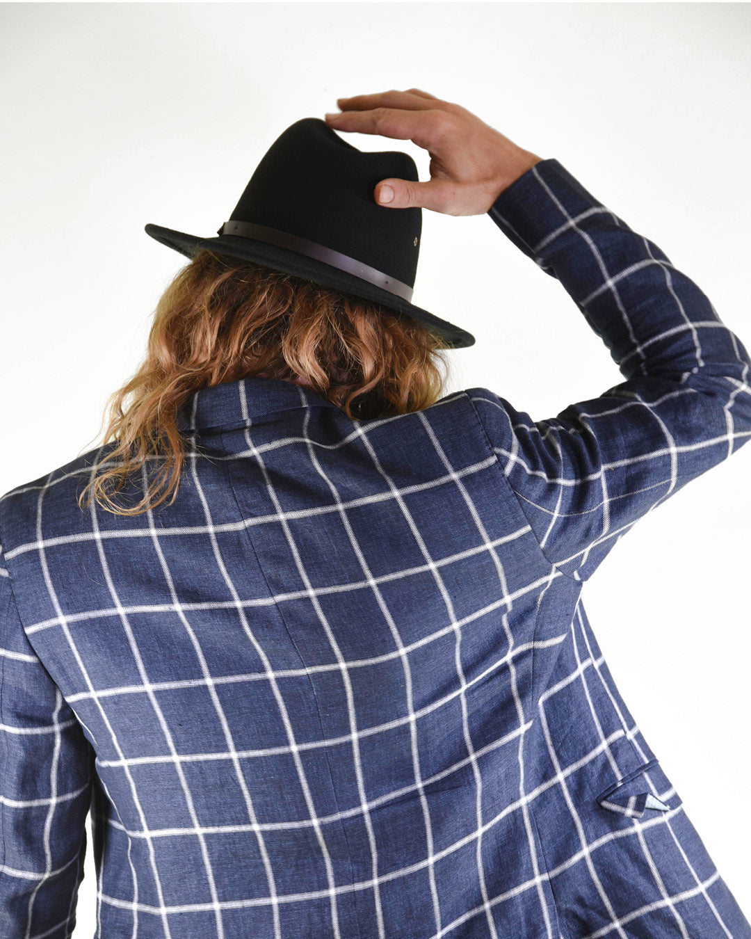 Person wearing a blue checkered jacket and black fedora, facing away from the camera.