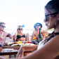 Group of friends wearing sunglasses enjoying a beachside lunch in full sun.