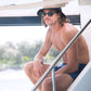 Model in swimwear and hat sitting on boat stairs wearing Dope Lemon sunglasses.