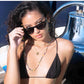 Model wearing black bikini and Dope Lemon sunglasses beside chrome bell on yacht.