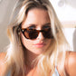 Close-up of woman wearing tortoise shell Dope Lemon sunglasses in soft lighting.
