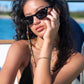 Female model wearing Dope Lemon sunglasses and gold chain on boat, hand resting on face.
