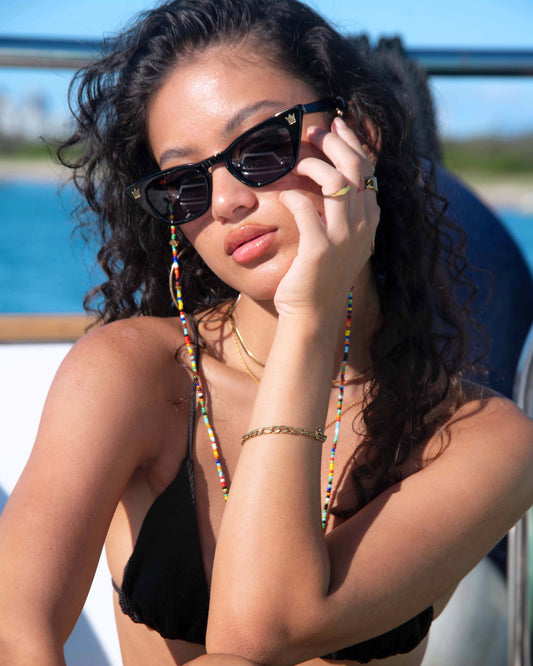 Female model wearing Dope Lemon sunglasses and gold chain on boat, hand resting on face.
