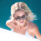 Model in white one-piece swimsuit and tortoise shell sunglasses, smiling in direct sun.