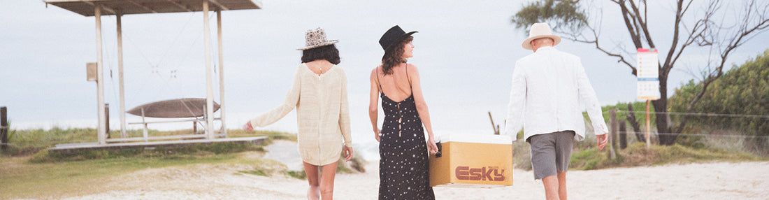 Two women and a man wearing Felt fedoras walk up a beach in Australia carrying an Esky. One woman is wearing a womens patterned felt hat, the other is wearing a black cowboy hat. The man is wearing a cream wool felt fedora
