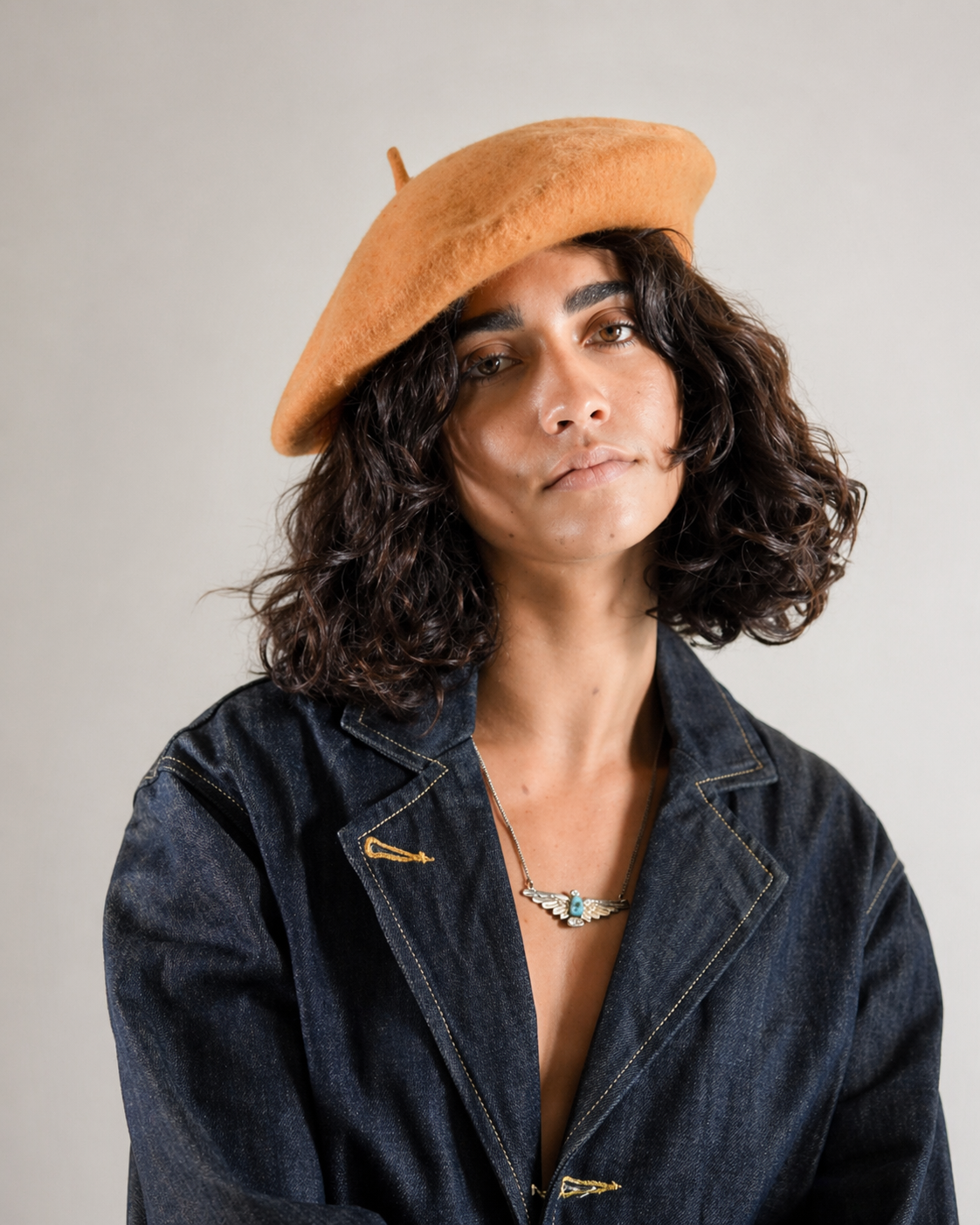 Person wearing a brown beret and denim jacket against a plain background