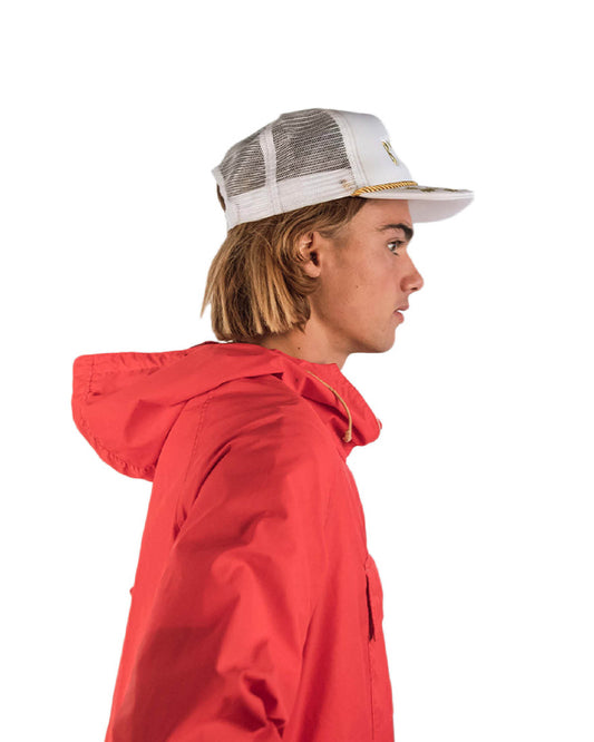 Lifestyle image of a male model wearing the Byron Trucker Cap in blue, styled with a red hoodie. The image shows the side profile of the cap’s structured fit and signature embroidery, embodying laid-back Byron energy.


