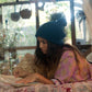 Indoor shot of model in soft lighting, wearing The Consciousness Beanie – Blue while journaling or drawing. A nod to comfort, creativity, and warmth.

