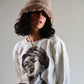Side-angled shot of the model adjusting the brim of The Cosmic Girl Bucket Hat in Tan Faux Fur. The faux fur texture is visibly plush, giving the hat a tactile and cozy finish. Perfect for cooler weather and effortless street style, captured in natural lighting for editorial appeal.

