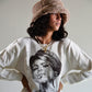 Model poses in profile with hands on hips while wearing The Cosmic Girl Bucket Hat in Tan Faux Fur. The image captures the depth of the crown and the soft curve of the brim, illustrating the hat’s warmth, comfort, and nostalgic aesthetic. A perfect unisex accessory for winter adventures or casual cosmic vibes.

