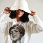 Model adjusting the brim of the white faux fur Cosmic Girl Bucket Hat. Styled with a graphic sweatshirt for a playful and nostalgic look, the soft bucket hat offers a cozy touch and fashion-forward silhouette.

