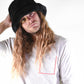 Person wearing a black hat and light gray shirt with a pink square design on a white background
