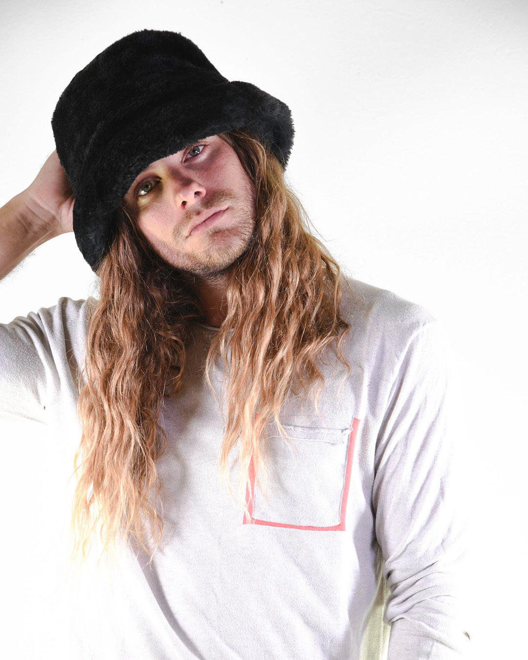 Person wearing a black hat and light gray shirt with a pink square design on a white background