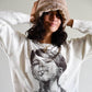Model wears The Cosmic Girl Bucket Hat in Tan Faux Fur with a relaxed pose, hands behind head. Styled with a graphic long-sleeve top, this image showcases the hat’s ultra-soft faux fur texture and everyday wearability. The neutral tan color complements winter layers and adds a nostalgic, cosmic feel to any outfit.

