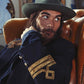 Man wearing a green wide-brim felt hat from the FBS x David Bromley collection sits in a vintage leather chair, dressed in a navy jacket with gold detailing. Captures the artistic, moody tone of the Fallenbrokenstreet collaboration campaign.