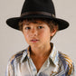 Child wearing a black fedora hat and patterned shirt against a neutral background